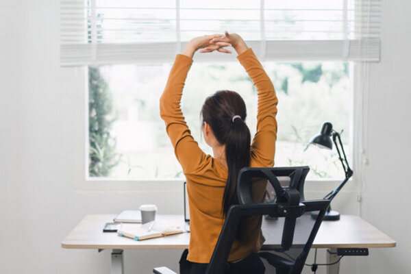 Person stretching arms while seated at a laptop in a bright room